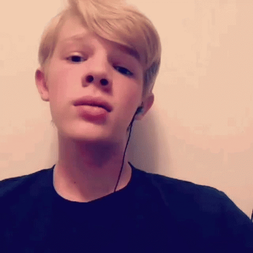 A Young Boy Wearing Headphones And A Black Shirt Is Making A Funny Face . GIF