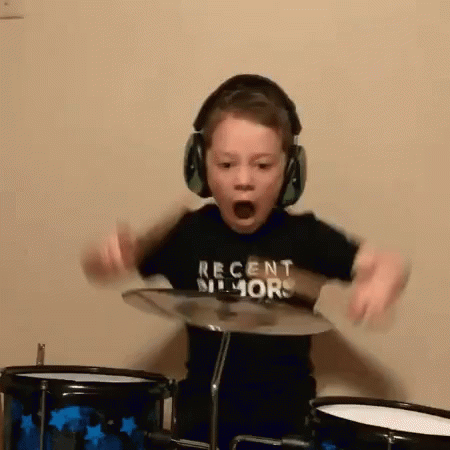 A Young Boy Wearing Headphones And A Shirt That Says Recent Humor Is Playing Drums . GIF