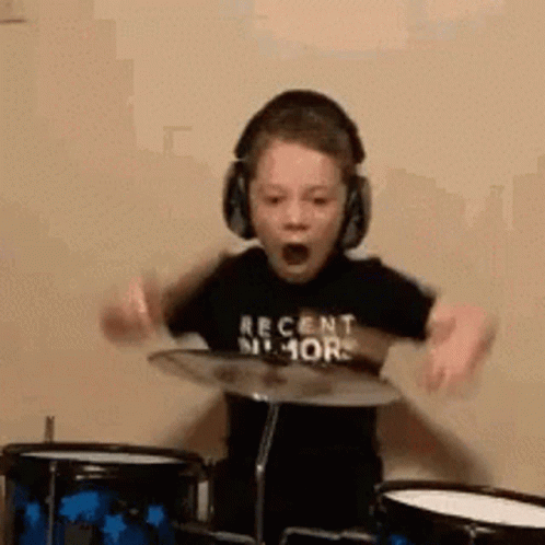 A Young Boy Wearing Headphones Is Playing Drums And Making A Funny Face . GIF