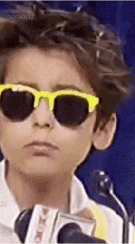A Young Boy Wearing Sunglasses And A Microphone . GIF