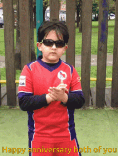A Young Boy Wearing Sunglasses Holds A Lollipop In Front Of A Fence With The Words Happy Anniversary Both Of You Written GIF