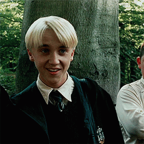 A Young Boy With Blonde Hair Is Wearing A Slytherin Uniform And Smiling GIF