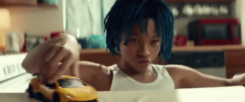 A Young Boy With Blue Hair Is Playing With A Toy Car On A Kitchen Counter . GIF