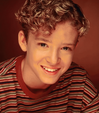 A Young Boy With Curly Hair Is Smiling For The Camera GIF