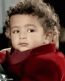 A Young Boy With Curly Hair Is Wearing A Red Jacket And Making A Funny Face . GIF