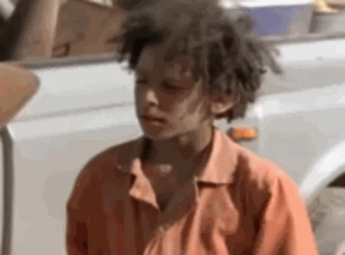 A Young Boy With Dreadlocks Is Standing Next To A White Truck . GIF