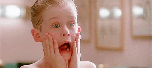 A Young Boy With His Mouth Open And His Hands On His Face Looks Surprised GIF