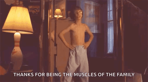 A Young Boy Without A Shirt Is Standing In A Room With His Hands On His Hips And A Lamp . GIF