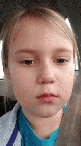 A Young Girl In A Blue Shirt Looks At The Camera With A Serious Look On Her Face GIF