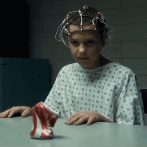 A Young Girl In A Hospital Gown Is Sitting At A Table With A Can Of Soda In Front Of Her GIF