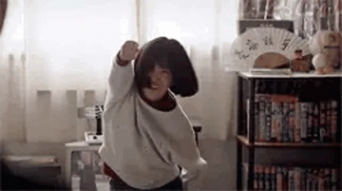 A Young Girl Is Dancing In A Room With A Fan . GIF