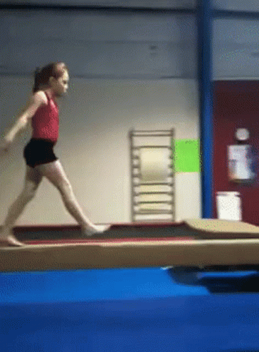 A Young Girl Is Doing A Trick On A Balance Beam In A Gym GIF