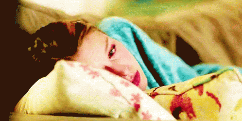 A Young Girl Is Laying On A Bed With A Blue Blanket On Her Head . GIF