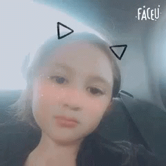 A Young Girl Is Sitting In A Car Wearing Cat Ears . GIF