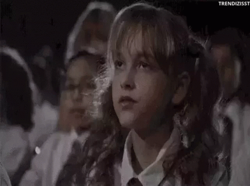 A Young Girl Is Sitting In A Crowd Of People Watching A Movie And Covering Her Mouth With Her Hand . GIF