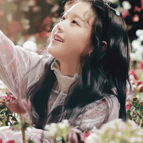 A Young Girl Is Standing In A Field Of Flowers Looking Up At The Sky . GIF