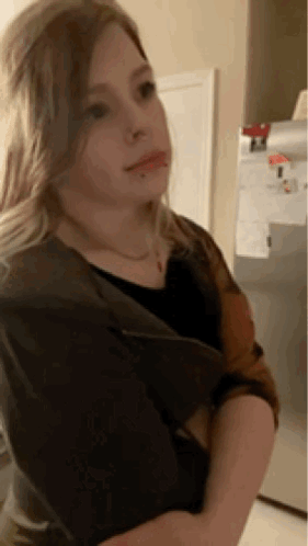 A Young Girl Is Standing In Front Of A Refrigerator And Looking At The Camera . GIF