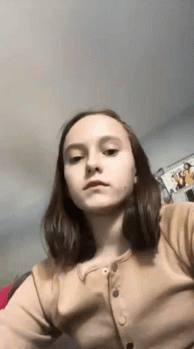 A Young Girl Is Taking A Selfie In A Room With A Picture On The Wall . GIF