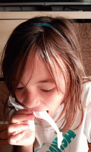 A Young Girl Wearing A Shirt That Says ' Hawaii ' On It Is Chewing On A Piece Of Paper GIF