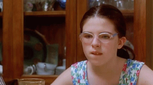 A Young Girl Wearing Glasses Is Sitting At A Table With A Glass Of Water GIF
