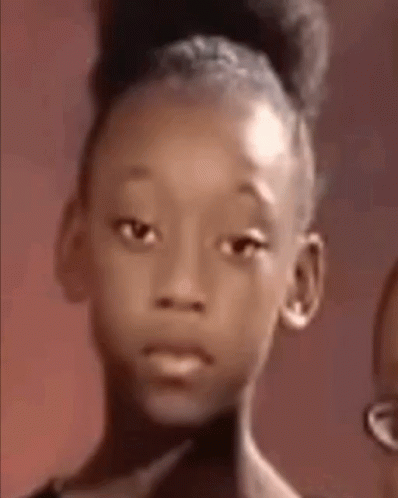 a young girl with a bun on her head is looking at the camera with a sad look on her face .