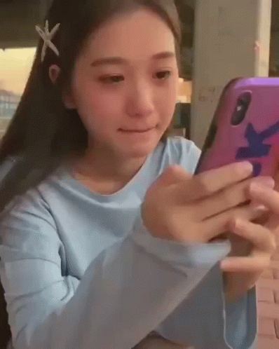 A Young Girl With A Starfish In Her Hair Is Looking At Her Cell Phone . GIF