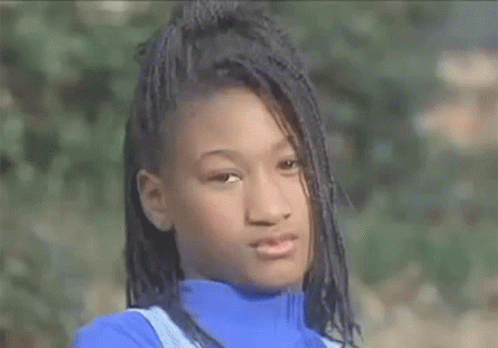 A Young Girl With Braids Is Wearing A Blue Turtleneck Sweater And Looking At The Camera . GIF