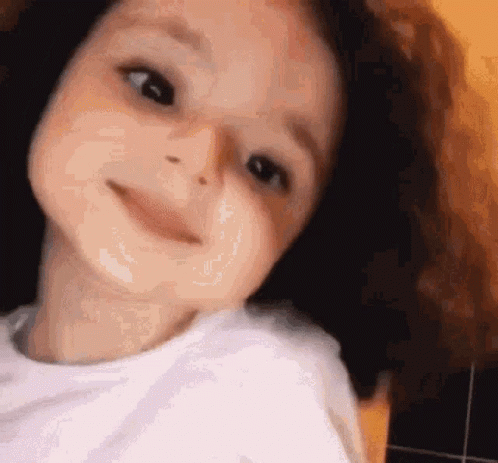 A Young Girl With Curly Hair Is Smiling For The Camera . GIF