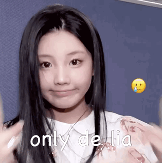 A Young Girl With Long Black Hair Is Smiling And Making A Funny Face While Wearing A White Shirt . GIF