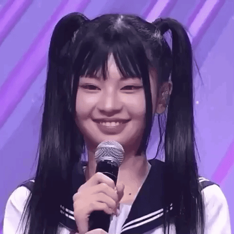 A Young Girl With Pigtails Is Smiling While Holding A Microphone . GIF