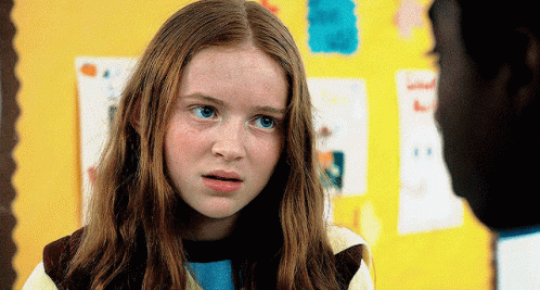 A Young Girl With Red Hair And Freckles Looks At A Man In Front Of A Yellow Wall GIF