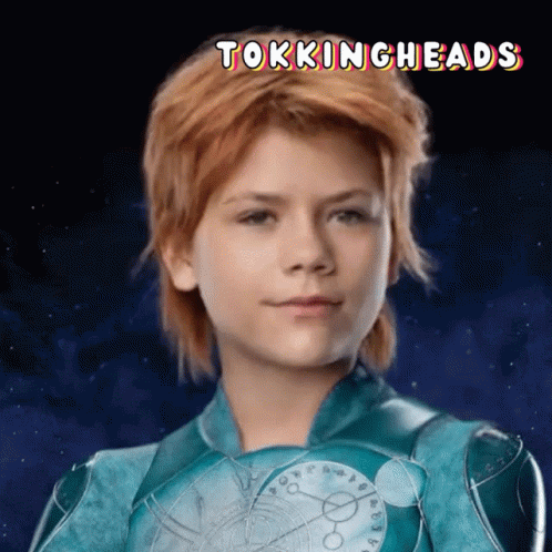 A Young Girl With Red Hair Is Wearing A Blue Superhero Costume With The Words Tokingheads Above Her GIF