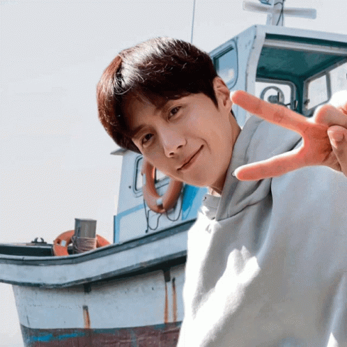 A Young Man Giving A Peace Sign With A Boat In The Background GIF