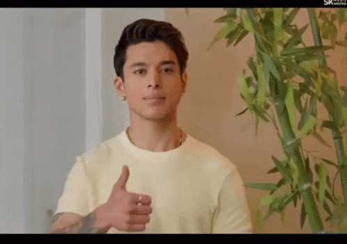 A Young Man Giving A Thumbs Up In Front Of A Bamboo Plant GIF