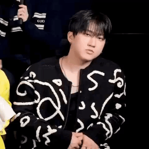 A Young Man In A Black And White Jacket Is Sitting In Front Of A Microphone . GIF