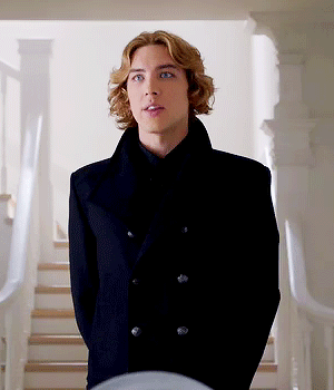 A Young Man In A Black Coat Is Standing In Front Of A Set Of Stairs GIF