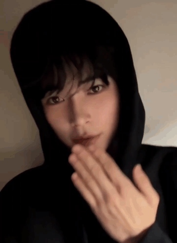 A Young Man In A Black Hoodie Is Blowing A Kiss GIF