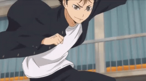 A Young Man In A Black Jacket And White Shirt Is Standing In Front Of A Building In A Karate Pose . GIF