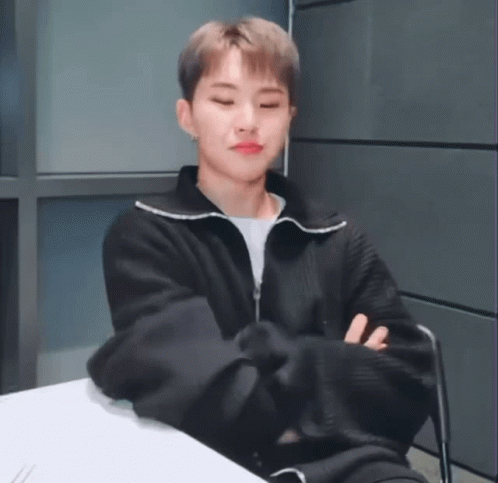 A Young Man In A Black Jacket Is Sitting At A Table With His Arms Crossed And His Eyes Closed . GIF