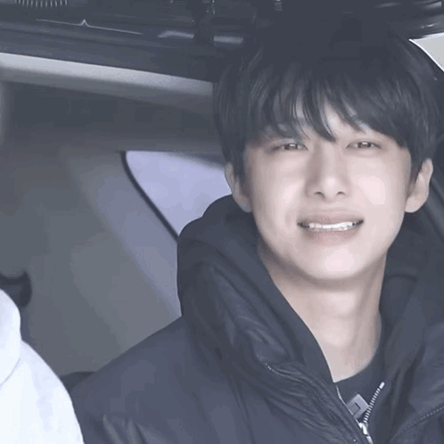 A Young Man In A Black Jacket Is Talking To Another Young Man In A Car GIF