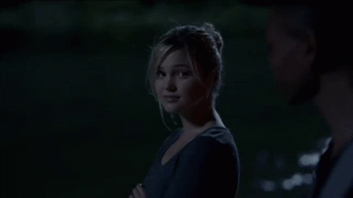 A Young Man In A Black Shirt And Gray Vest Is Standing In The Dark . GIF