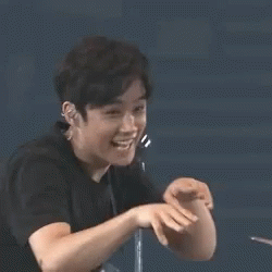 A Young Man In A Black Shirt Is Making A Funny Face With His Hand . GIF