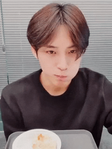 A Young Man In A Black Shirt Is Sitting At A Table With A Bowl Of Food . GIF
