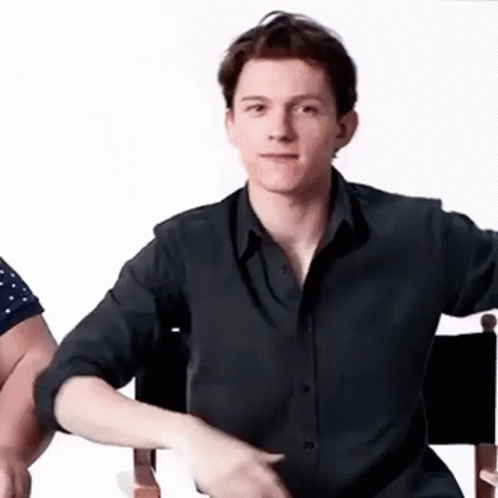 A Young Man In A Black Shirt Is Sitting In A Chair And Making A Funny Face . GIF