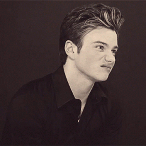 A Young Man In A Black Shirt Is Smiling GIF