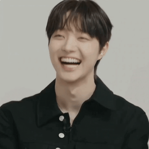 A Young Man In A Black Shirt Is Smiling And Looking At The Camera GIF