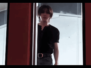 A Young Man In A Black Shirt Is Standing In A Doorway . GIF
