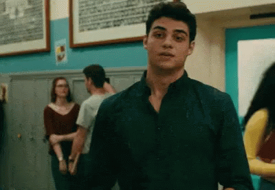 A Young Man In A Black Shirt Is Standing In A Hallway With Other People . GIF