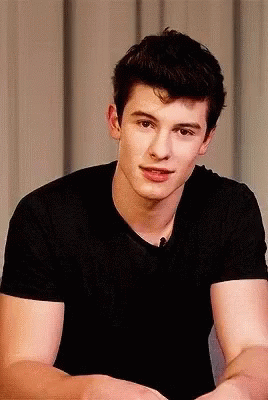 A Young Man In A Black Shirt Looks At The Camera With His Arms Crossed GIF