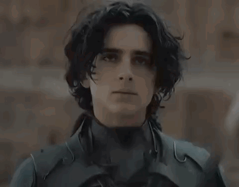 a young man in a black suit is holding a sword in his hand .